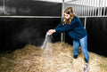 Person sprinkling Sandezia Bedding drying powder into horse stall bedding