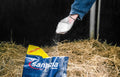 Person sprinkling a sandezia bedding powder from Sandezia Farms in a livestock stall