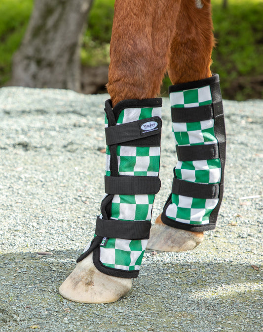 Horse leg with green and white checkered protective boot on a gravel surface.